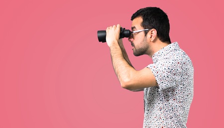 Handsome man with glasses with binoculars on pink backgroundの写真素材
