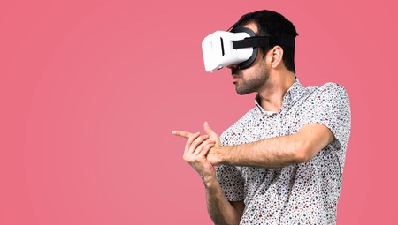 Handsome man with glasses using VR glasses on pink background
