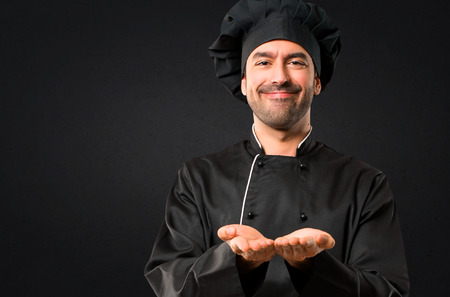 Chef man In black uniform holding copyspace imaginary on the palm to insert an ad on black backgroundの写真素材