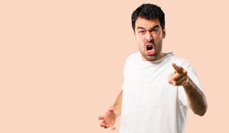 Young man with white shirt annoyed angry in furious gesture. Frustrated by a bad situation and pointing to the front on isolated ocher backgroundの写真素材