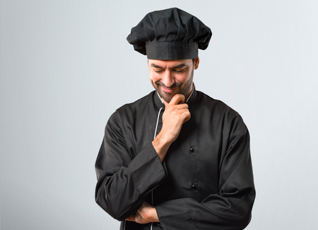 Chef man In black uniform standing and looking down with the hand on the chin on grey backgroundの写真素材