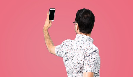 Handsome man with glasses making a selfie on pink backgroundの写真素材