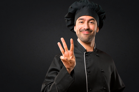 Chef man In black uniform happy and counting three with fingers on black backgroundの写真素材