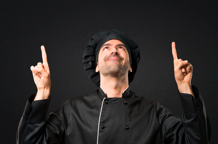 Chef man In black uniform pointing with the index finger a great idea and looking up on black backgroundの写真素材