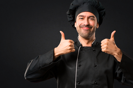 Chef man In black uniform giving a thumbs up gesture and smiling because has had success on black backgroundの写真素材