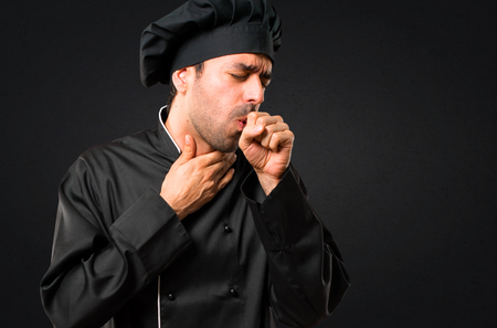 Chef man In black uniform is suffering with cough and feeling bad on black backgroundの写真素材