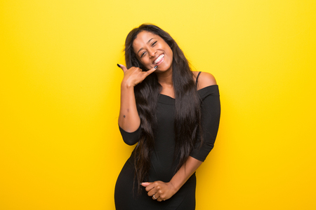 Young afro american woman on vibrant yellow background making phone gesture. Call me back signの写真素材