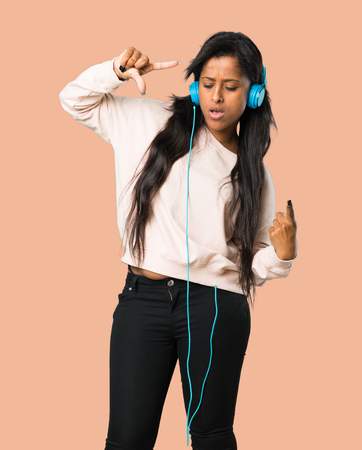 Young afro american woman listening to music with headphones and dancing on isolated brown backgroundの写真素材