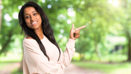 Young afro american woman pointing finger to the side in lateral position at outdoorsの写真素材