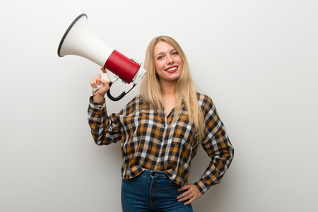 Blonde young girl over white wall holding a megaphoneの写真素材