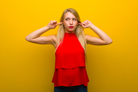 Young girl with red dress over yellow wall covering both ears with handsの写真素材