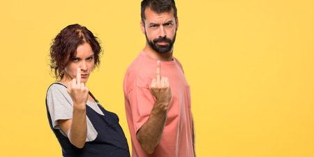 Couple with pregnant woman making horn gesture. Negative expression on isolated yellow background