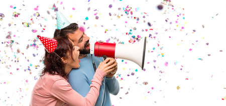 couple with birthday hats and holding a megaphone with confetti in a partyの写真素材