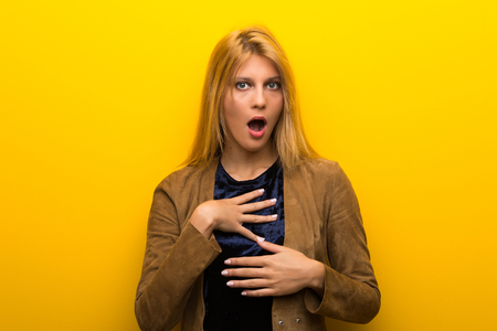 Blonde girl on vibrant yellow background surprised and shocked while looking rightの写真素材