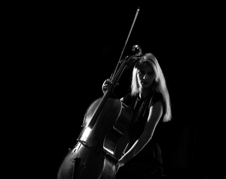 Young girl playing the cello on isolated black backgroundの写真素材