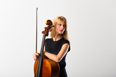 Young blonde girl with her cello posing on white wallの写真素材