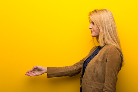 Blonde girl on vibrant yellow background handshaking after good dealの写真素材