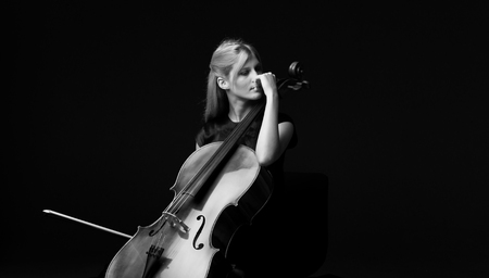 Young girl playing the cello on isolated black backgroundの写真素材