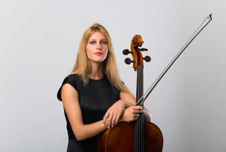 Young blonde girl with her cello posing on white wallの写真素材