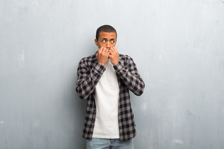 Young african american man with checkered shirt is a little bit nervous and scared putting hands to mouthの写真素材