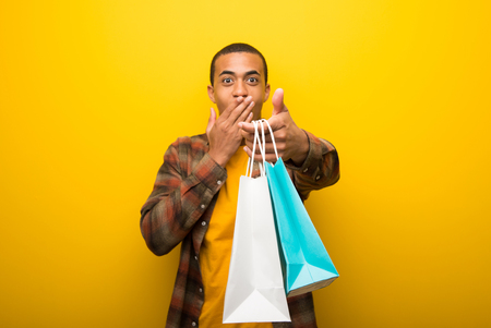 Young african american man on vibrant yellow background surprised while holding a lot of shopping bagsの写真素材