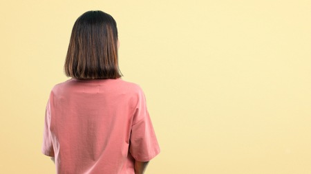 Young girl with pink shirt looking back on yellow background