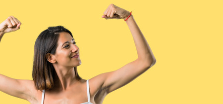 Sport woman making strong gesture on yellow backgroundの写真素材