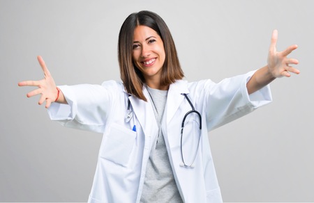 Doctor woman with stethoscope presenting and inviting to come with hand. Happy that you came on grey backgroundの写真素材