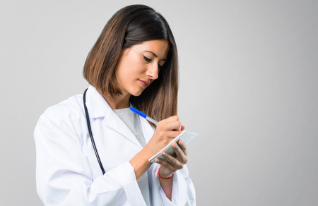 Doctor woman with stethoscope holding a notebook on grey backgroundの写真素材