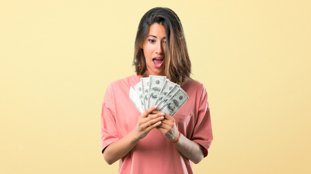 Surprised Young girl with pink shirt taking a lot of money on yellow backgroundの写真素材