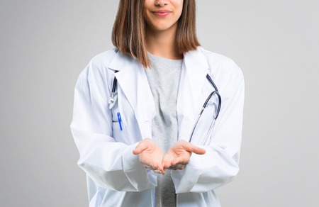 Doctor woman with stethoscope holding copyspace imaginary on the palm to insert an ad on grey backgroundの写真素材