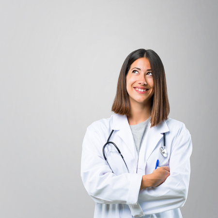 Doctor woman with stethoscope stand and looking up while smiling on grey backgroundの写真素材