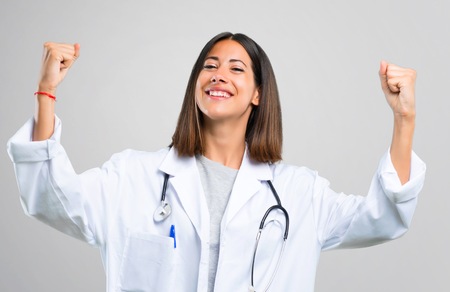 Doctor woman with stethoscope celebrating a victory in winner position on grey backgroundの写真素材
