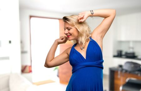Pregnant blonde woman with blue dress listening to the music and dancing in her houseの写真素材