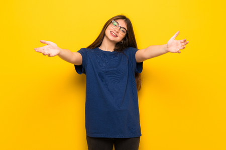 Young woman with glasses over yellow wall presenting and inviting to come with handの写真素材
