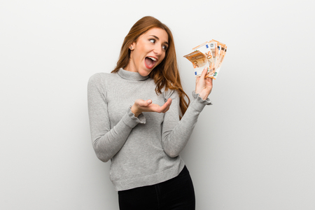 Redhead girl over white wall taking a lot of moneyの写真素材