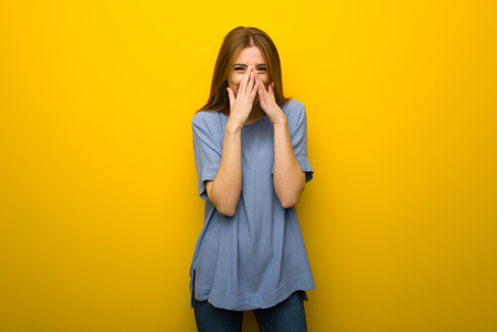 Young redhead girl over yellow wall background smiling a lot while covering mouthの写真素材