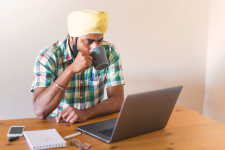 Indian with turban working with his laptop and  holding a cup of coffeeの写真素材