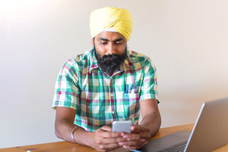 Indian with turban working with his laptop and using mobile phone