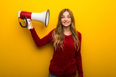 Young girl on vibrant yellow background taking a megaphone that makes a lot of noiseの写真素材