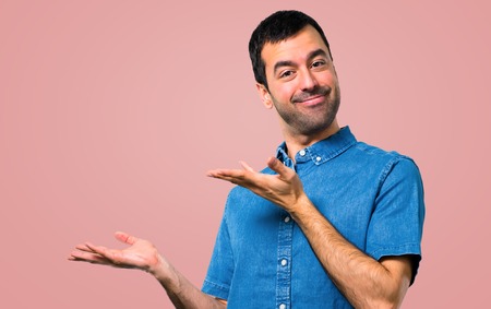 Handsome man with blue shirt presenting and inviting to come on pink backgroundの写真素材