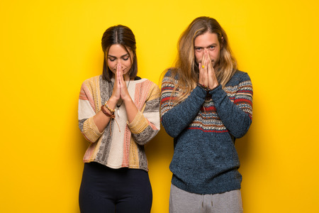 Hippie couple over yellow background keeps palm together. Person asks for somethingの写真素材