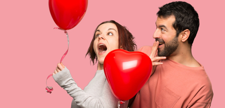 Couple in valentine day with balloons with heart shape over isolated pink backgroundの写真素材