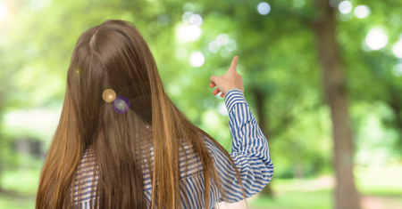 Young girl with striped shirt pointing back with the index finger at outdoorsの写真素材