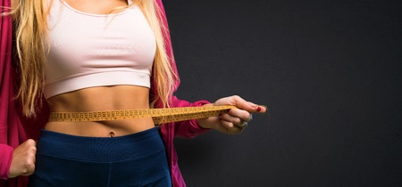 Pretty sport woman with tape measure on textured black backgroundの写真素材