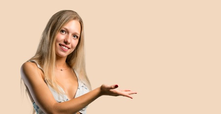 Young blonde woman presenting a product or an idea while looking smiling towards on ocher backgroundの写真素材