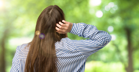 Young girl with striped shirt on back position looking back while scratching head at outdoorsの写真素材