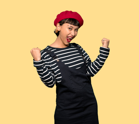 Young woman with beret celebrating a victory over yellow backgroundの写真素材