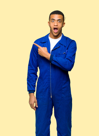 Young afro american worker man surprised and pointing side on isolated backgroundの写真素材