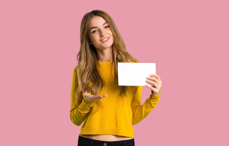 young girl with yellow sweater holding an empty placard for insert a concept on isolated pink backgroundの写真素材